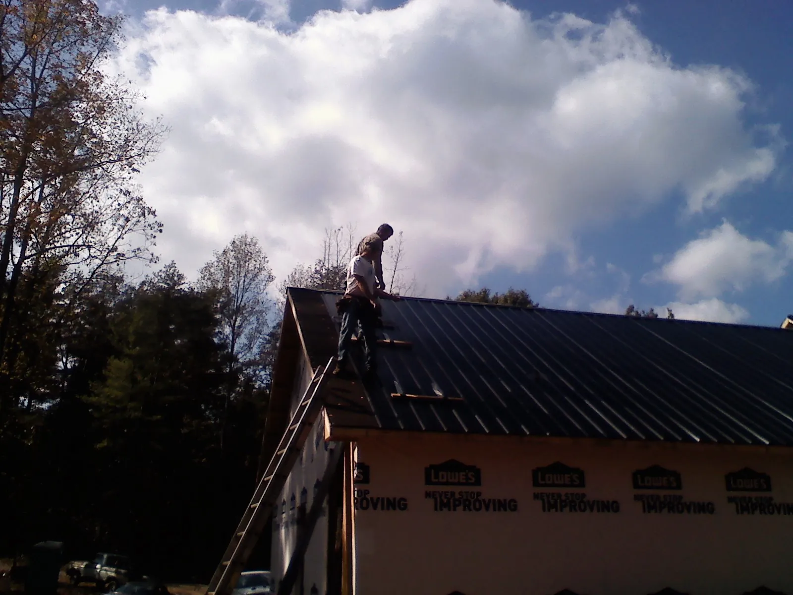 Roofer fastening dark metal panels high against a cloudy sky, from a Roof Inspection job in Garrison