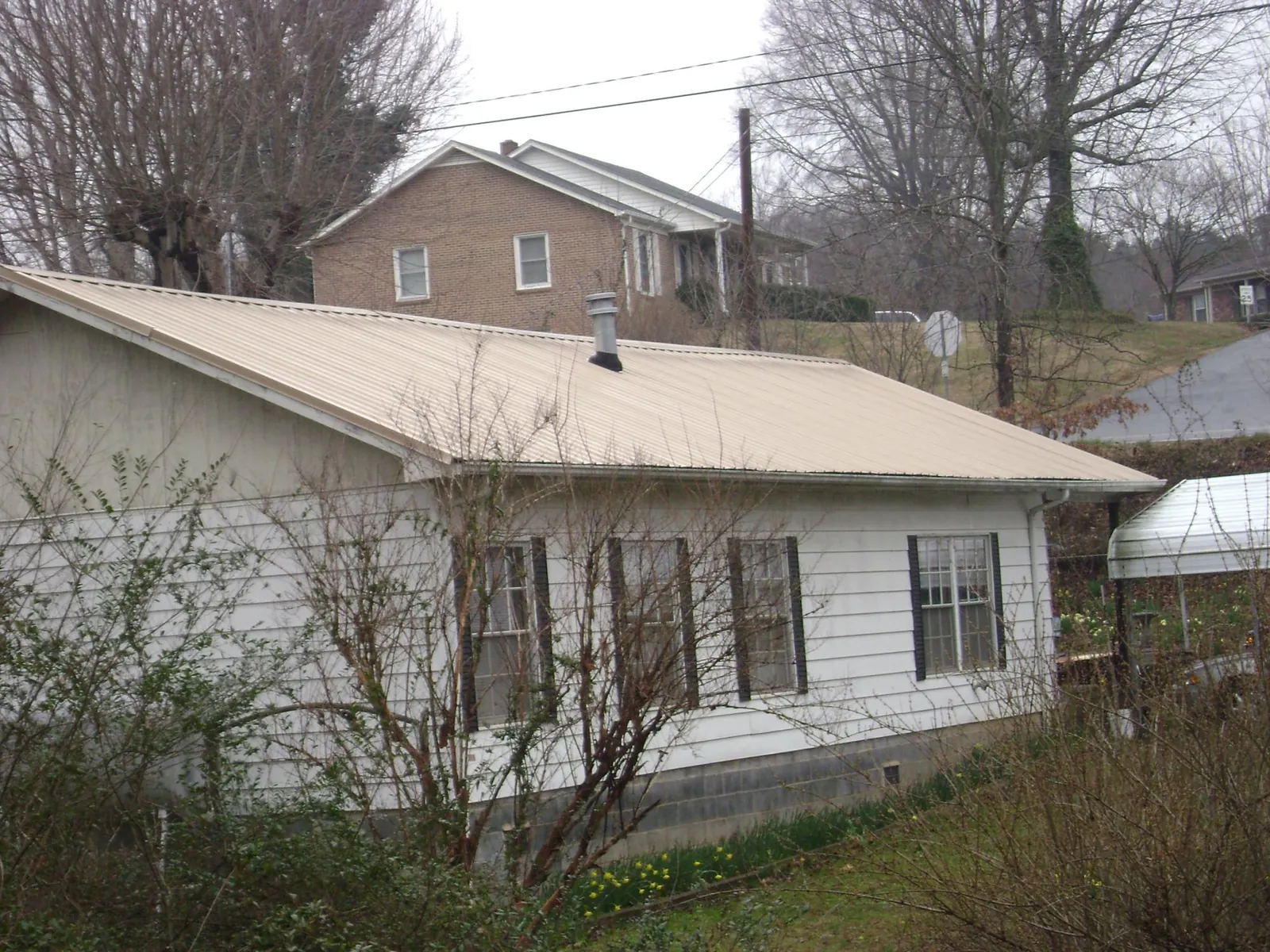 Tan metal roof on a white sided house set into a hillside — Commercial Roofing by Roofing Brothers in Garrison